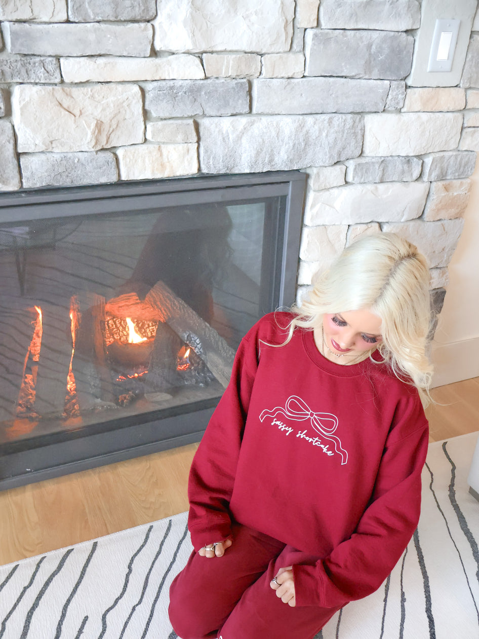 Burgundy sweatpants from Sassy Shortcake, modeled on figure, featuring an elastic waist, pockets, and white bow accents.