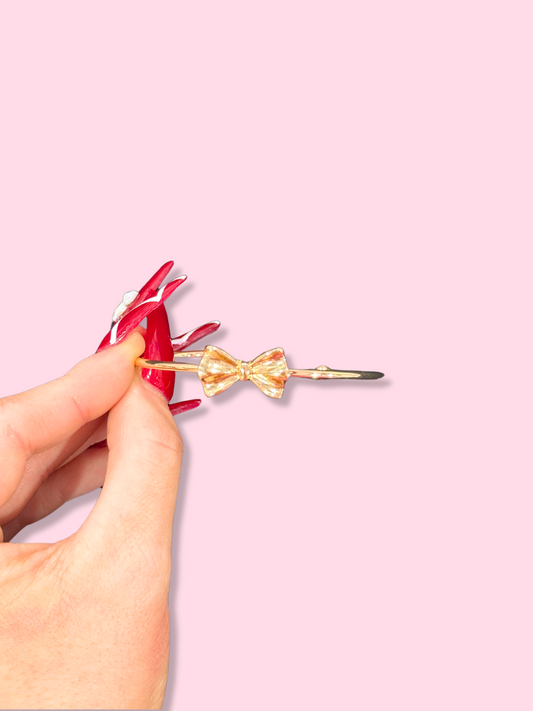 Gold bow bangle bracelet on a hand against a pink background