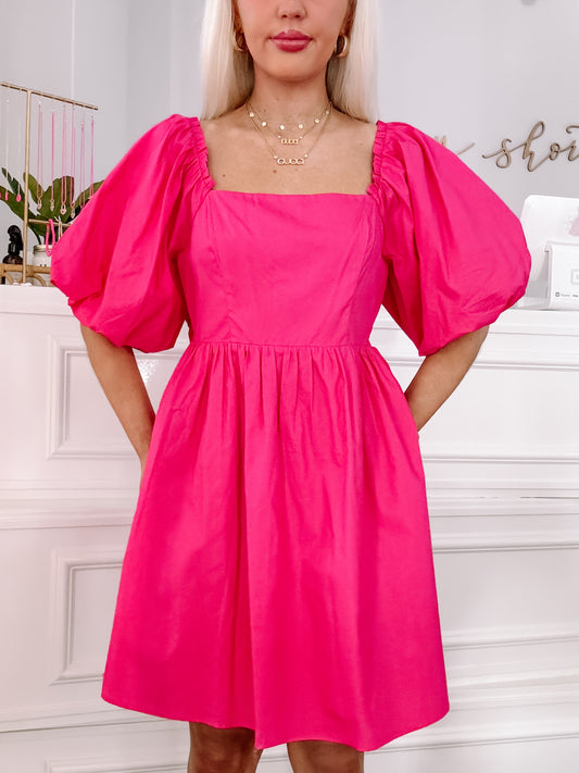 Hot pink mini dress with puffed sleeves and a square neckline, shown on a model.
