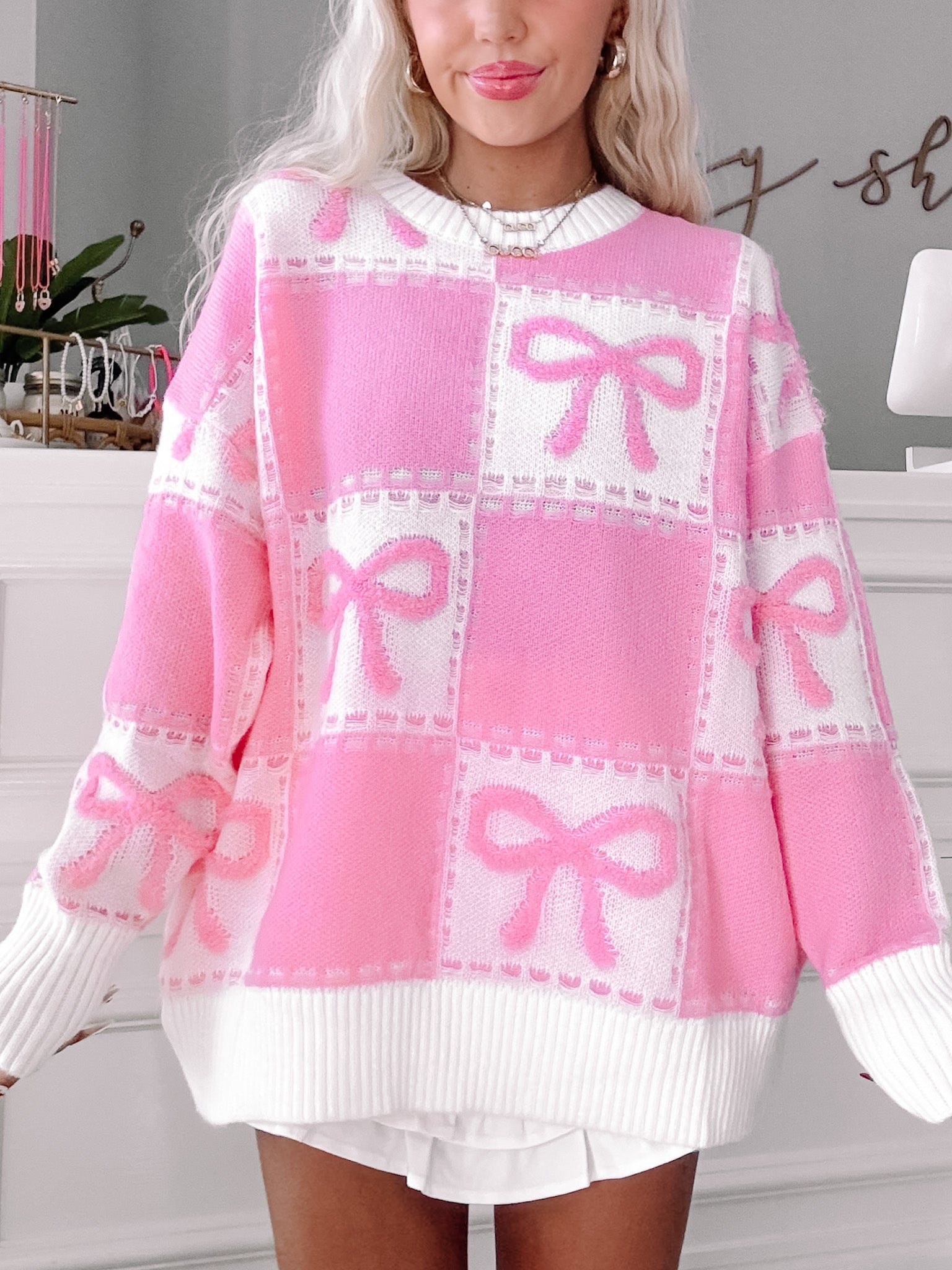 Pink and white knit sweater featuring a playful bow pattern, shown on a model.
