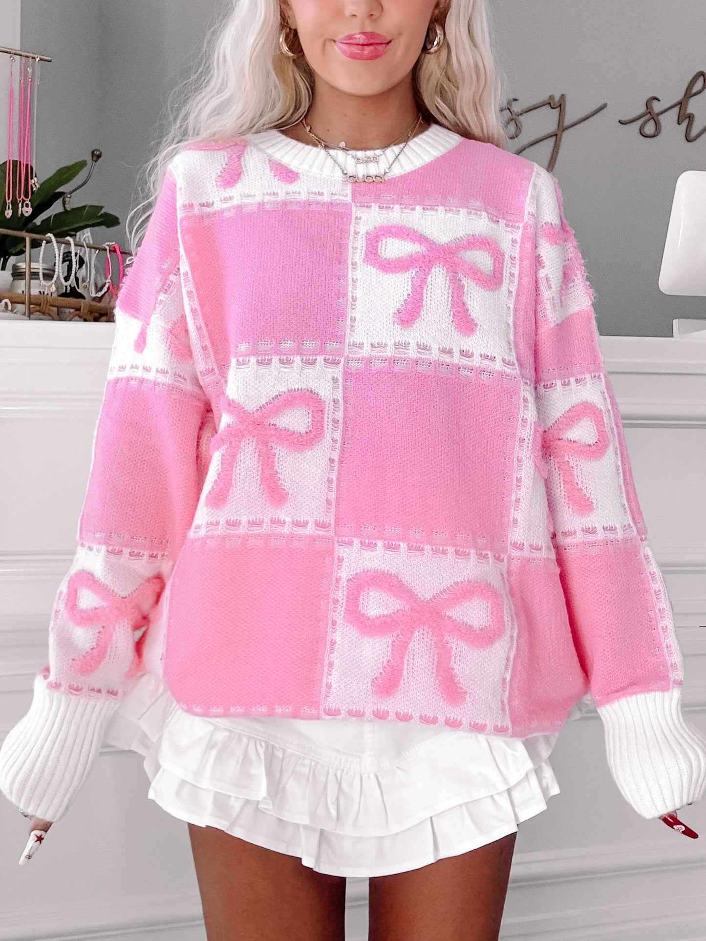 Pink knit sweater featuring a playful bow pattern, shown on a model.
