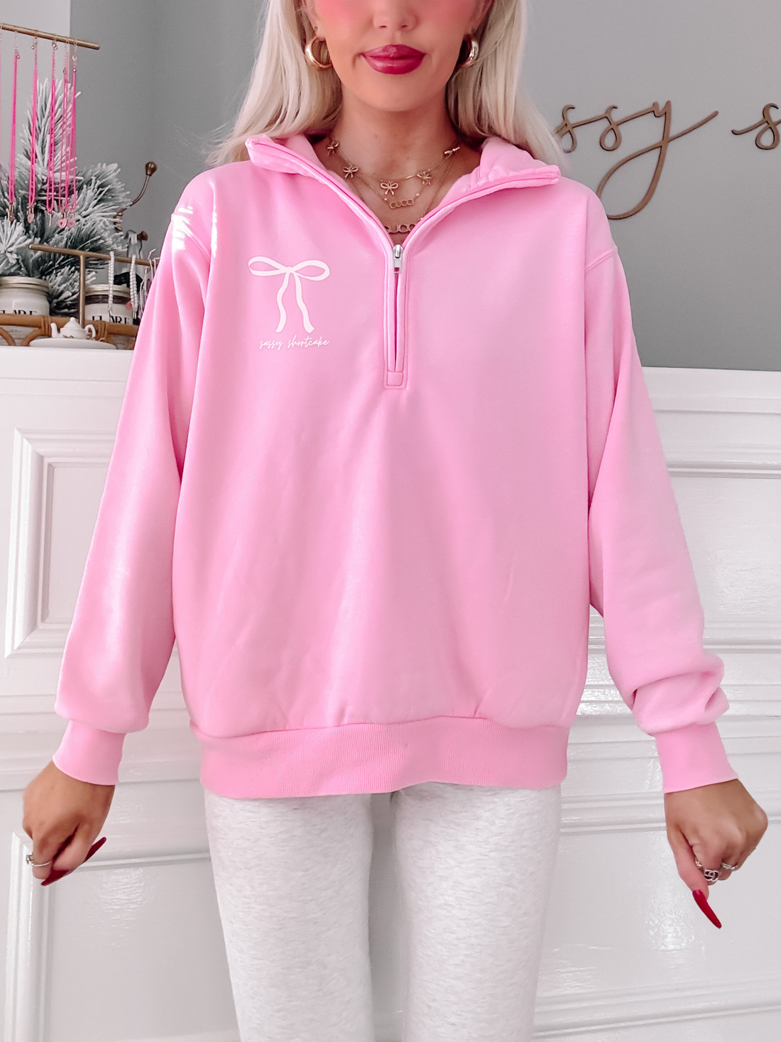 Pink quarter-zip sweatshirt with bow detail, modeled against a white background.
