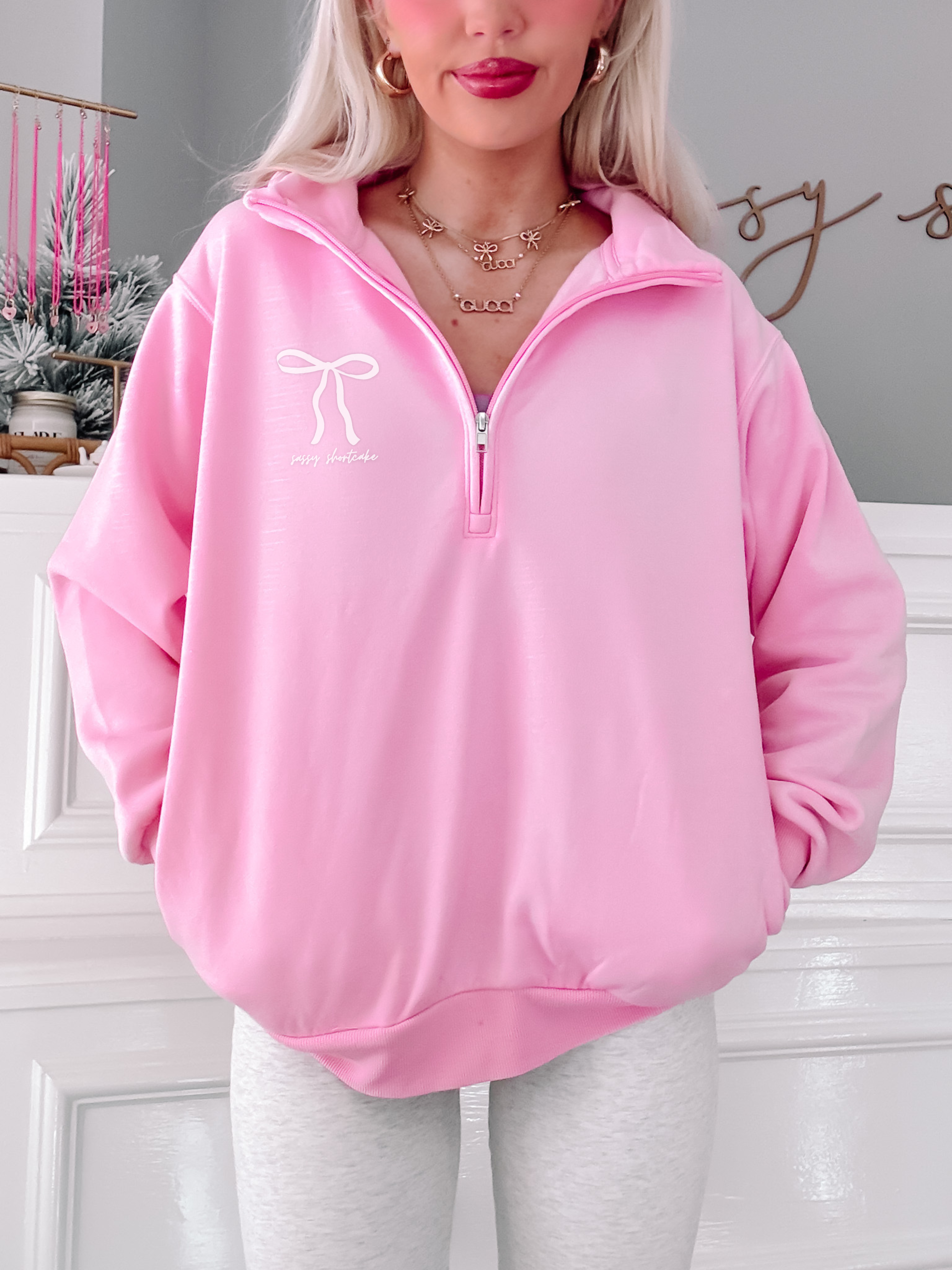 Pink quarter-zip sweatshirt with bow detail, modeled against a white background.
