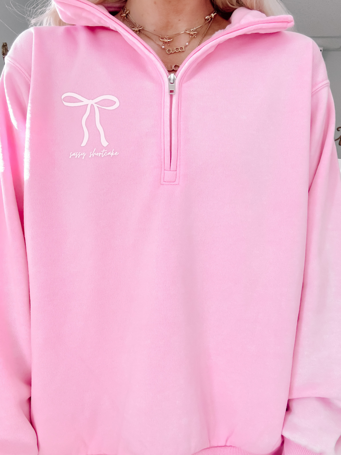 Pink quarter-zip sweatshirt with bow detail and “sassy shortcake” text.
