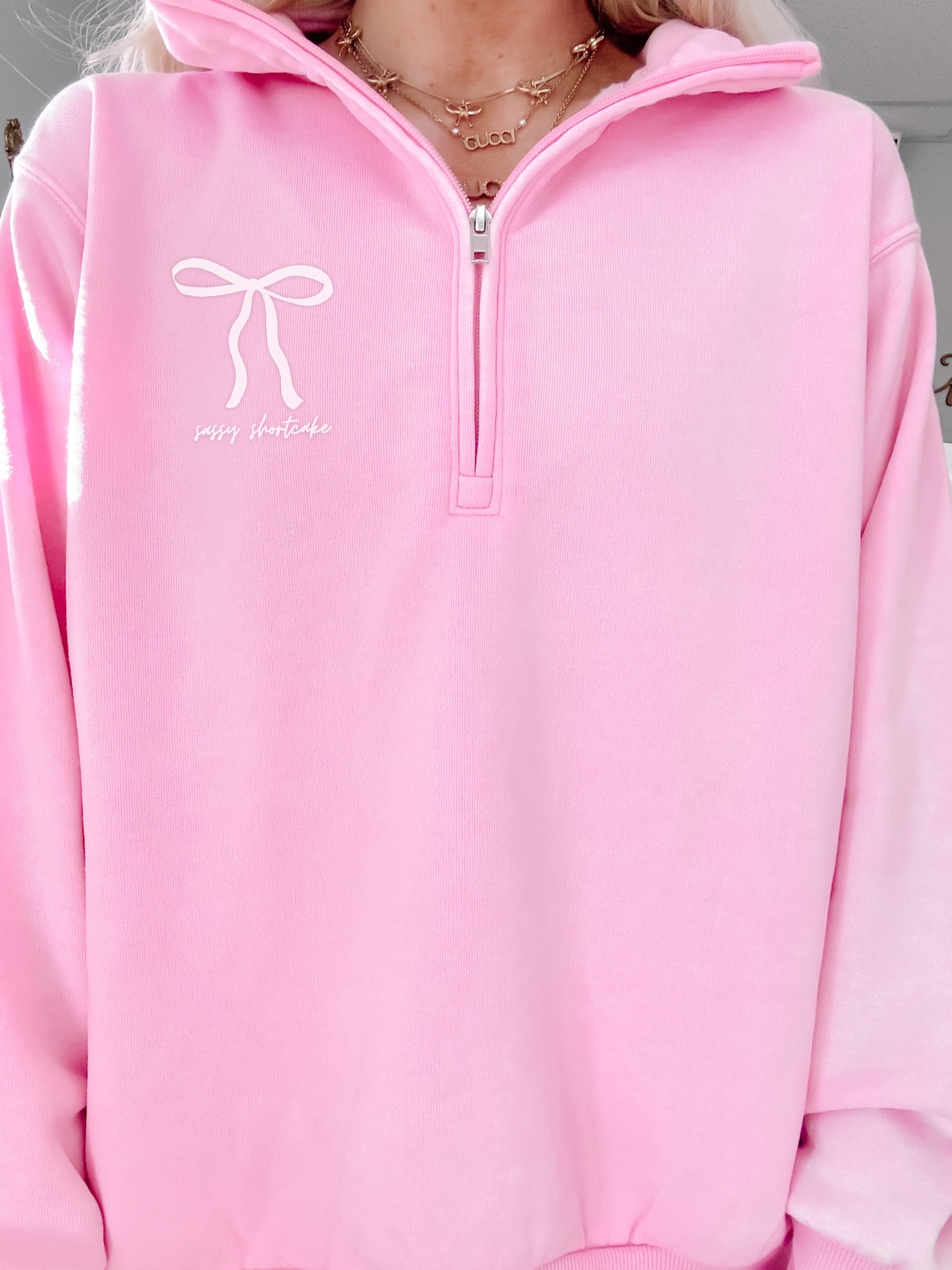 Pink quarter-zip sweatshirt with a bow graphic and 