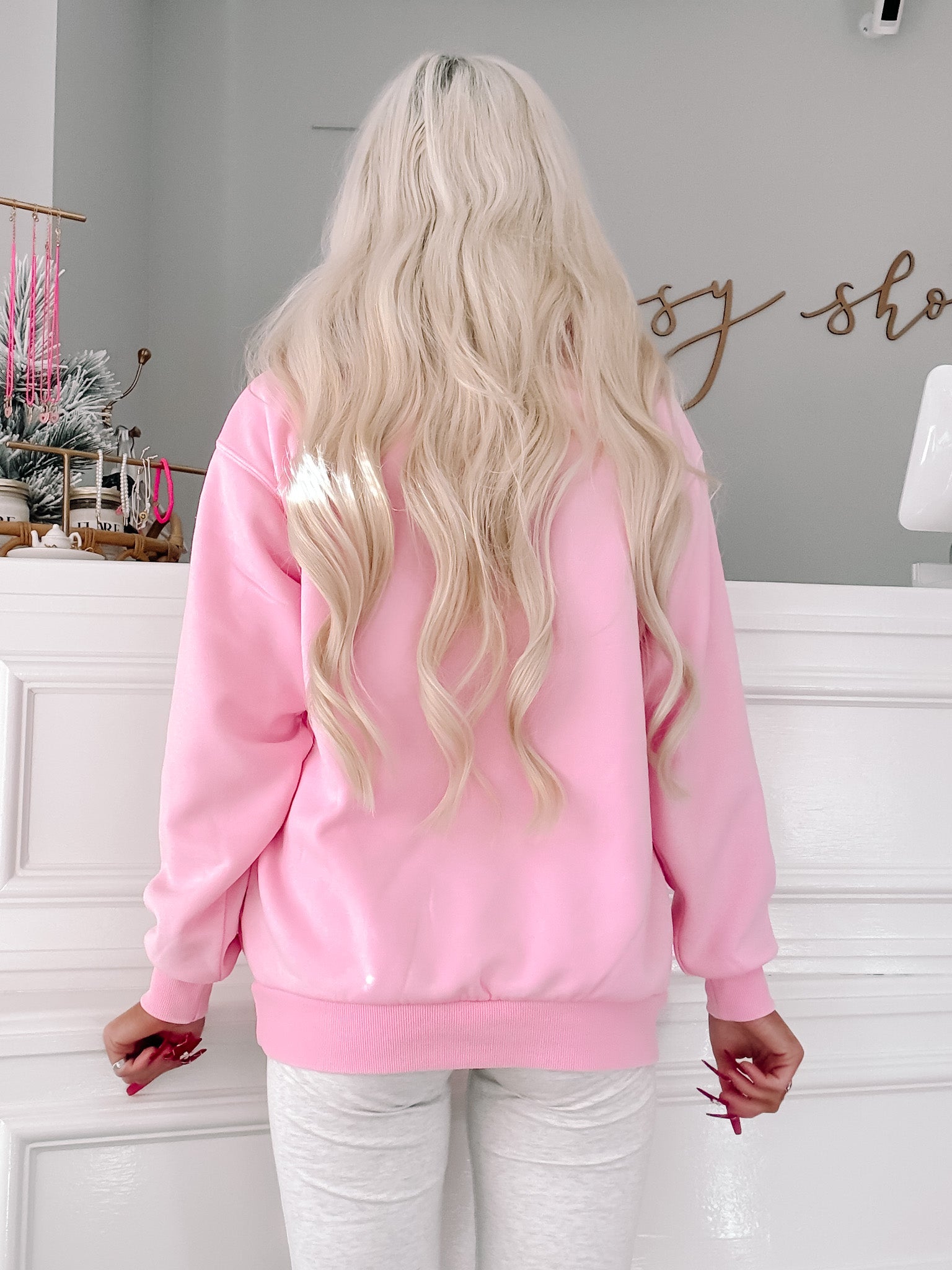 Pink quarter-zip sweatshirt styled with grey joggers, shown from the back.
