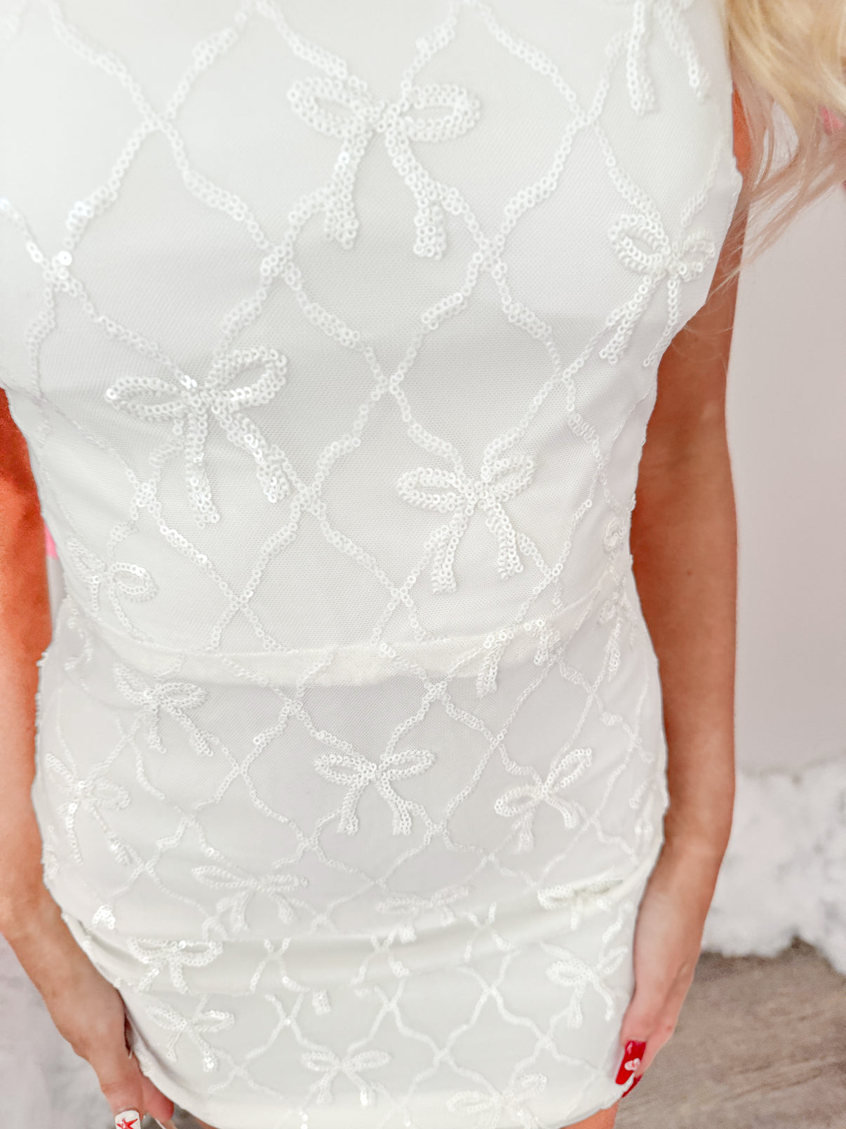 Close-up of white mini dress, adorned with sequined bows in a lattice pattern.
