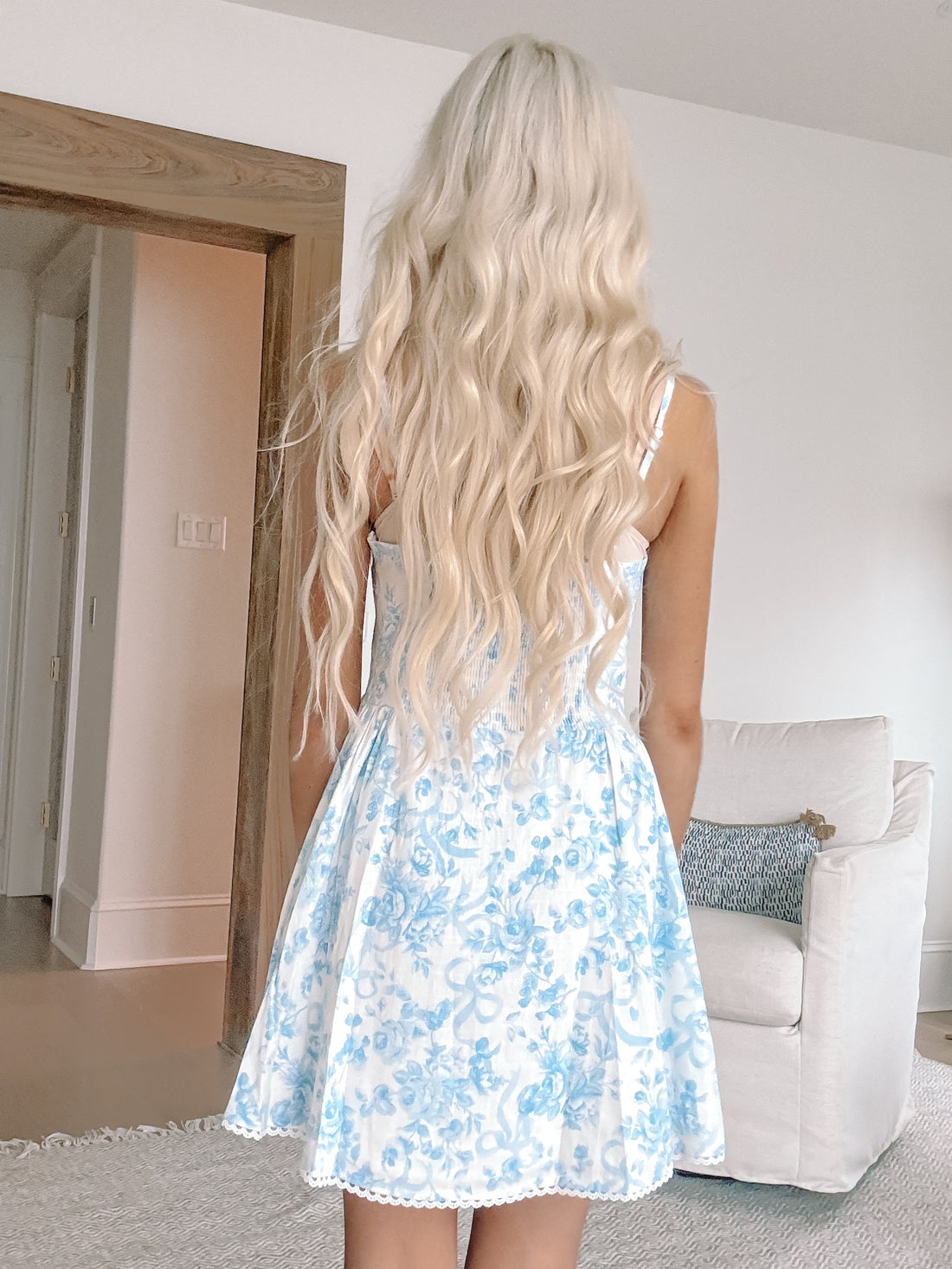 Blue floral mini dress with ribbon print, shown from the back in a home setting.
