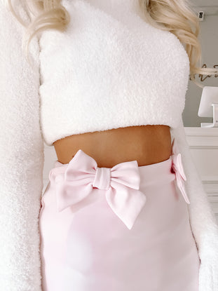 Pink mini skirt with large bow detail, worn with a fluffy white sweater.
