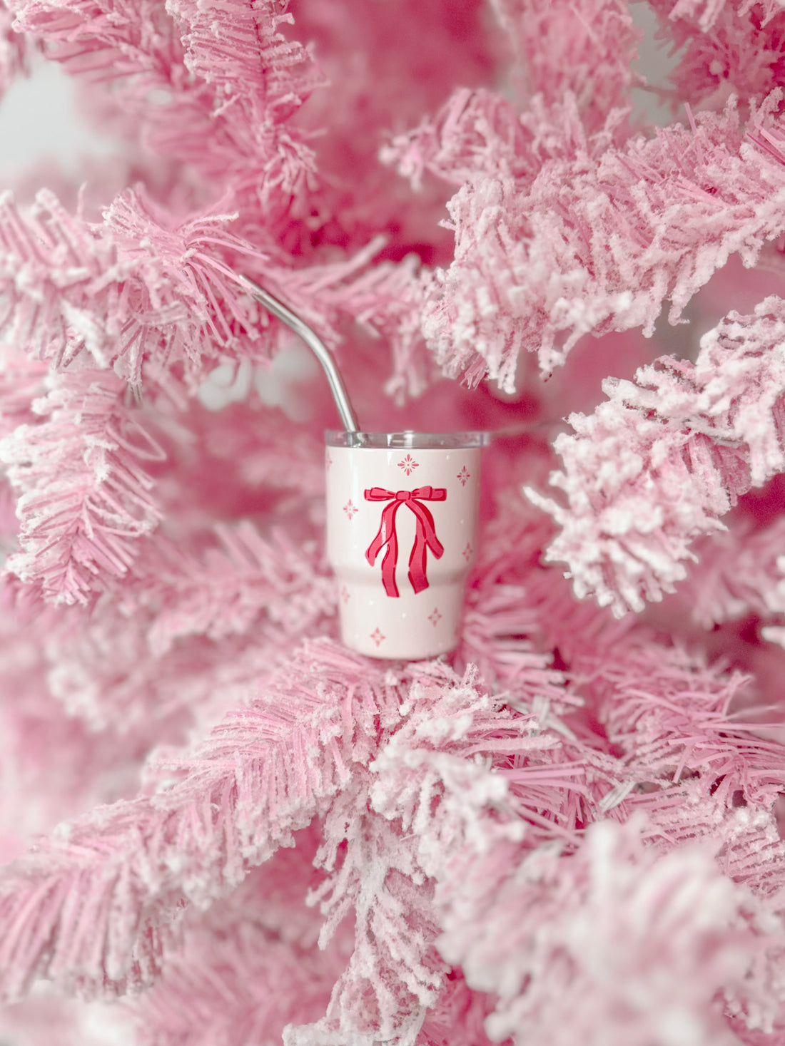 Pink tumbler with bow design nestled in a fluffy pink tree.
