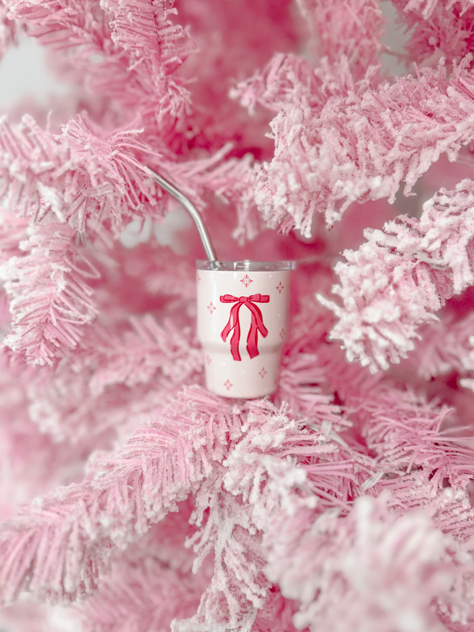 Pink tumbler with bow design nestled in a fluffy pink tree.
