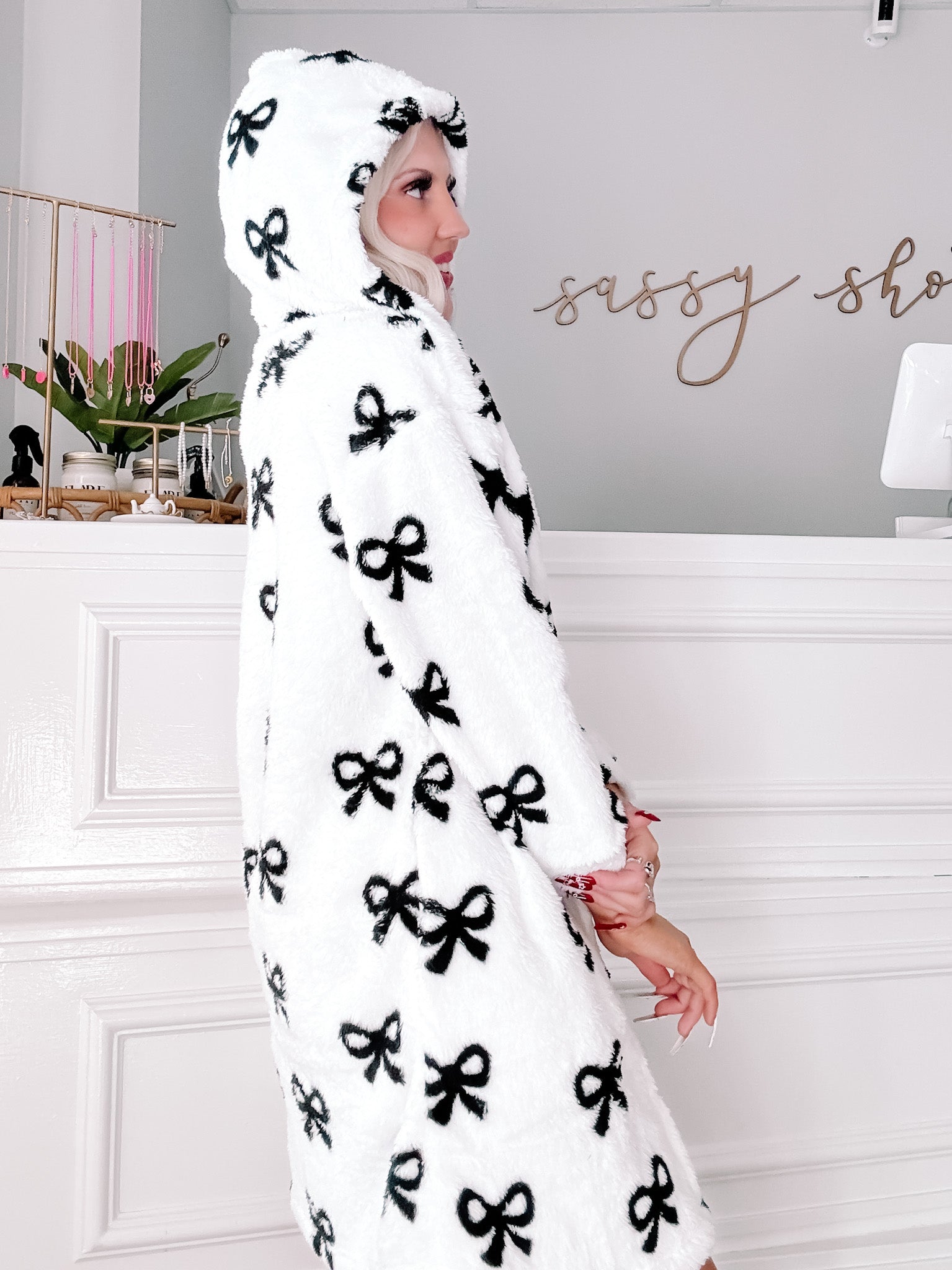 White hooded pajama coat with black bow print, shown in a boutique setting.
