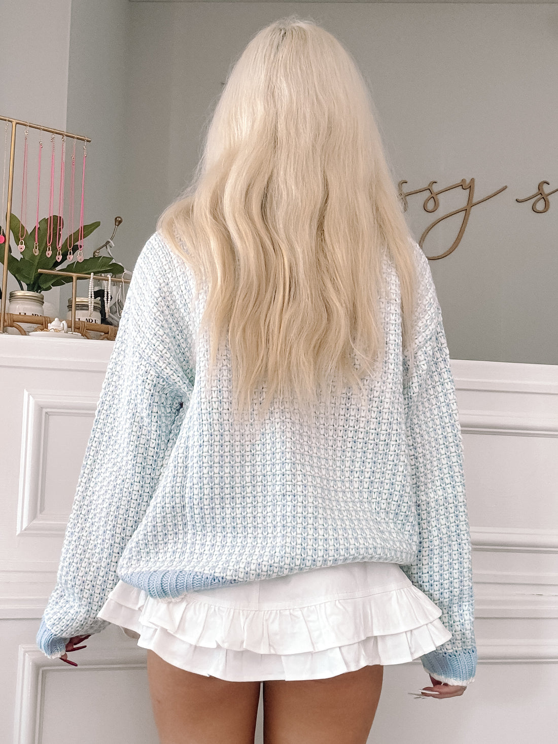 Light blue knit sweater, textured pattern, shown from the back against a white wall.
