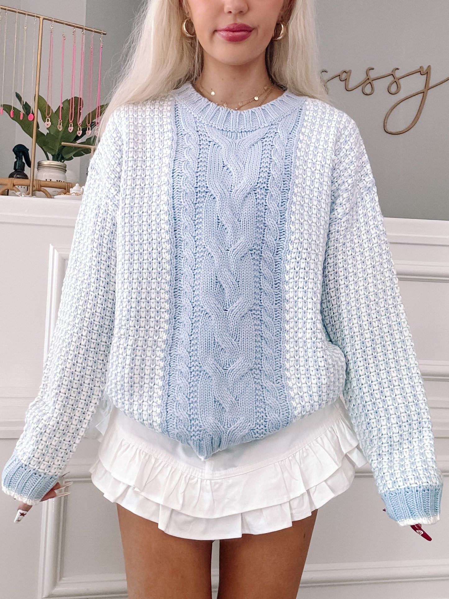 Light blue cable knit sweater with white accents, styled with a white ruffle skirt.
