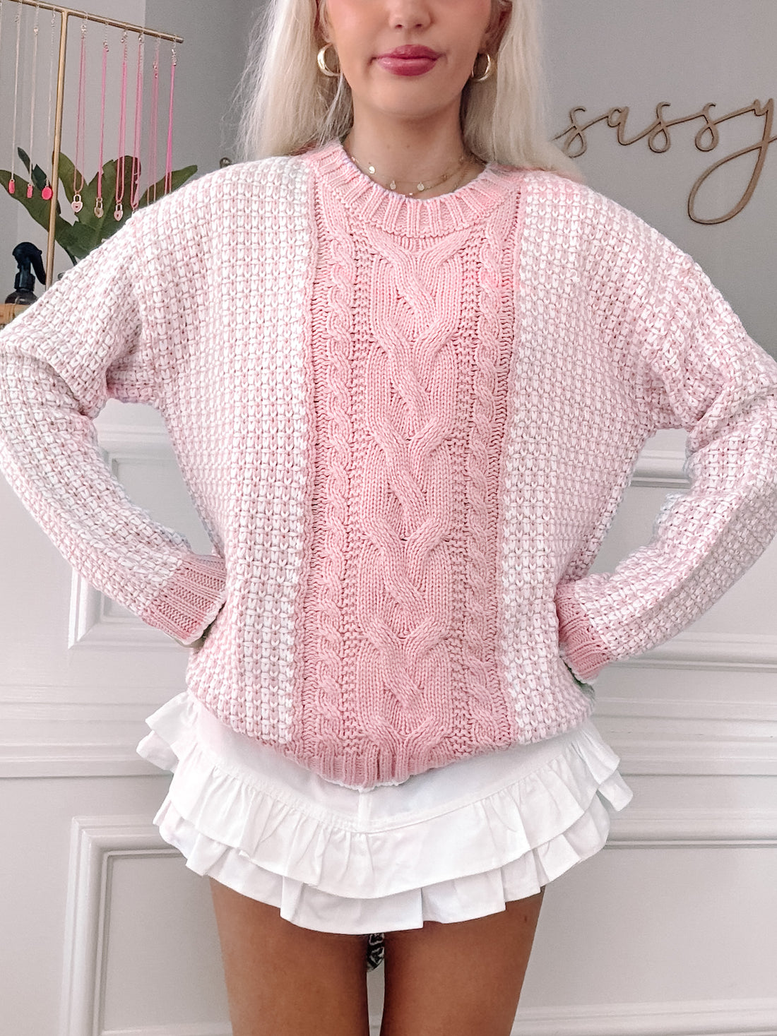 Pink and white cable-knit sweater with textured detailing, styled with a ruffled white skirt.
