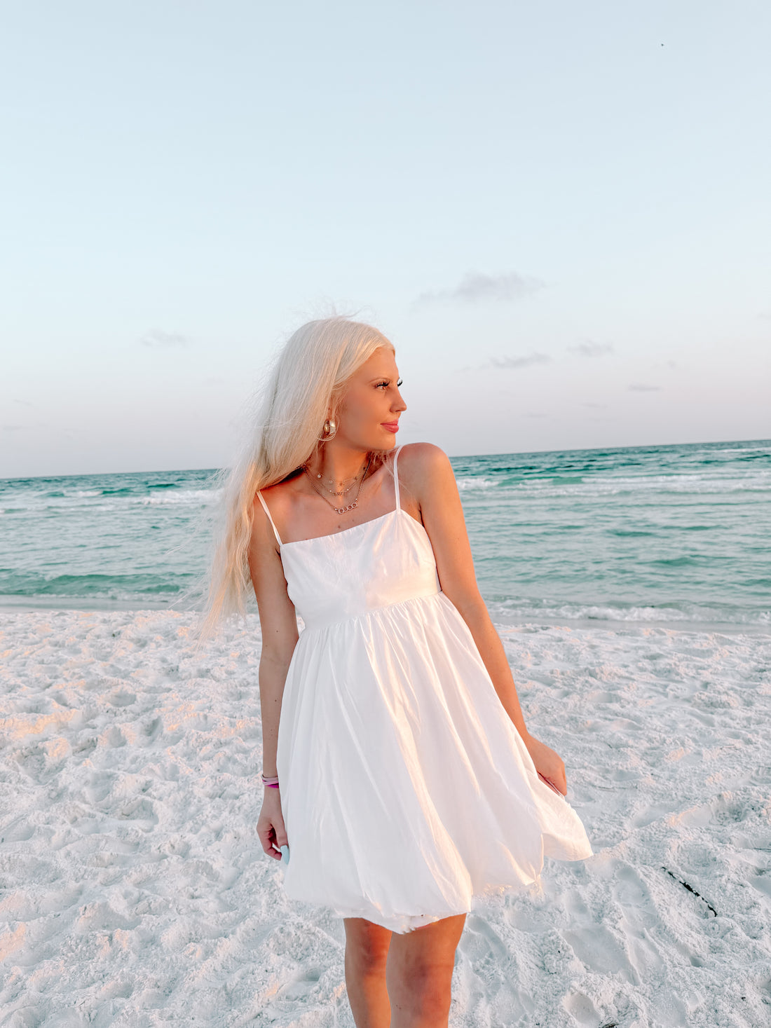 Woman in white sundress on a sandy beach at sunset.
