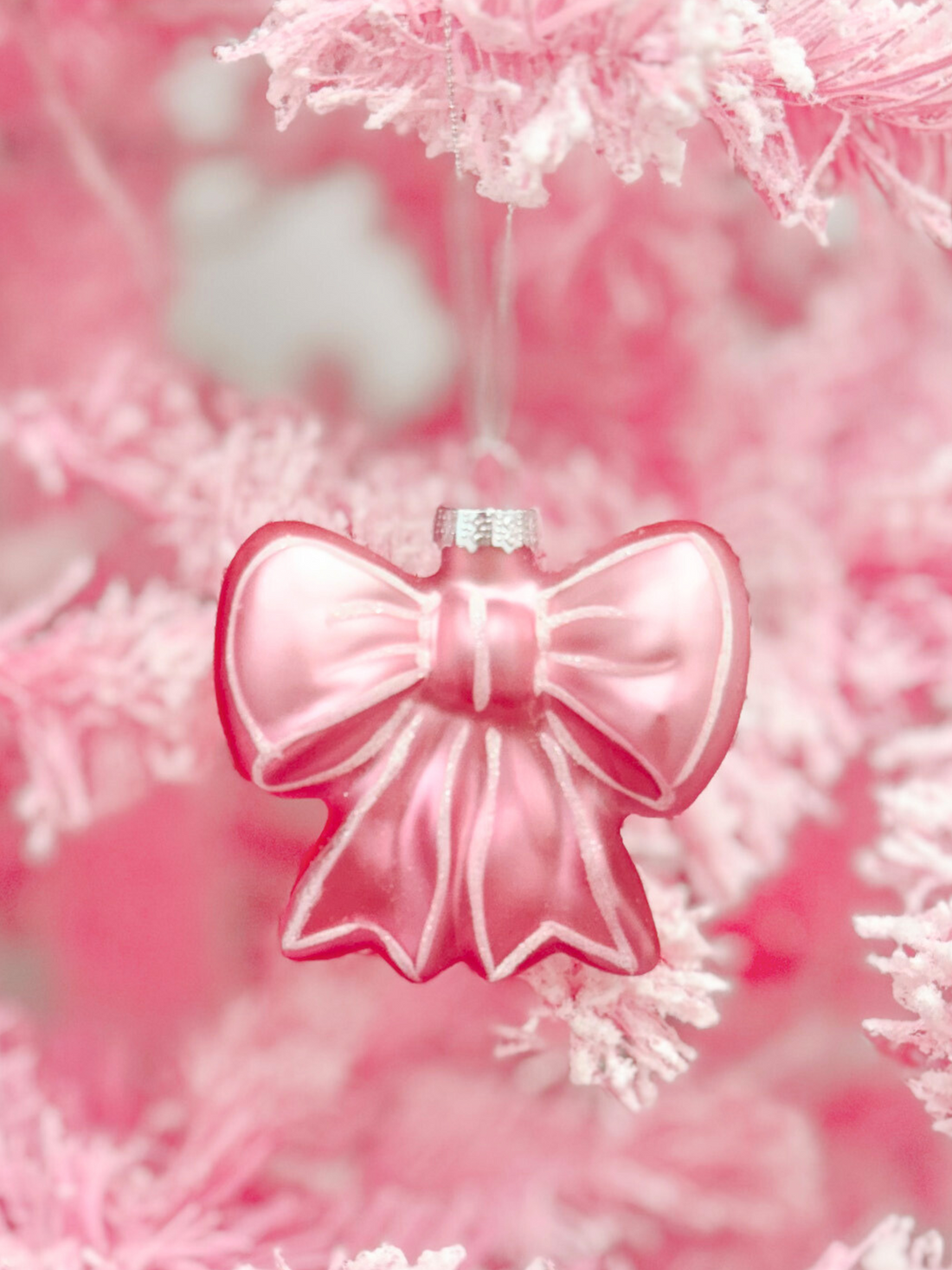 Pink glass bow ornament hanging on a frosted pink Christmas tree.
