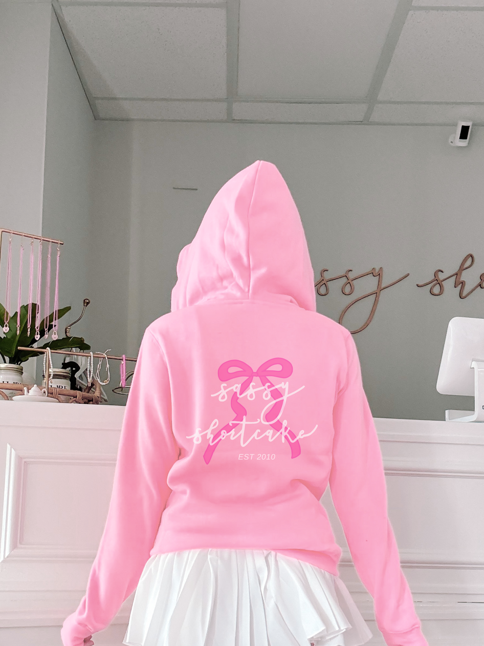 Pink hoodie with bow and text detail, shown from the back.
