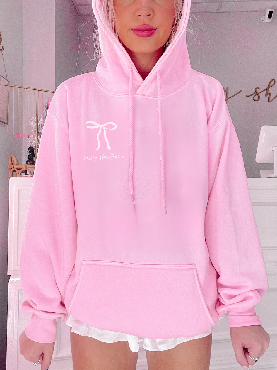Pink hoodie featuring a bow and text graphic.
