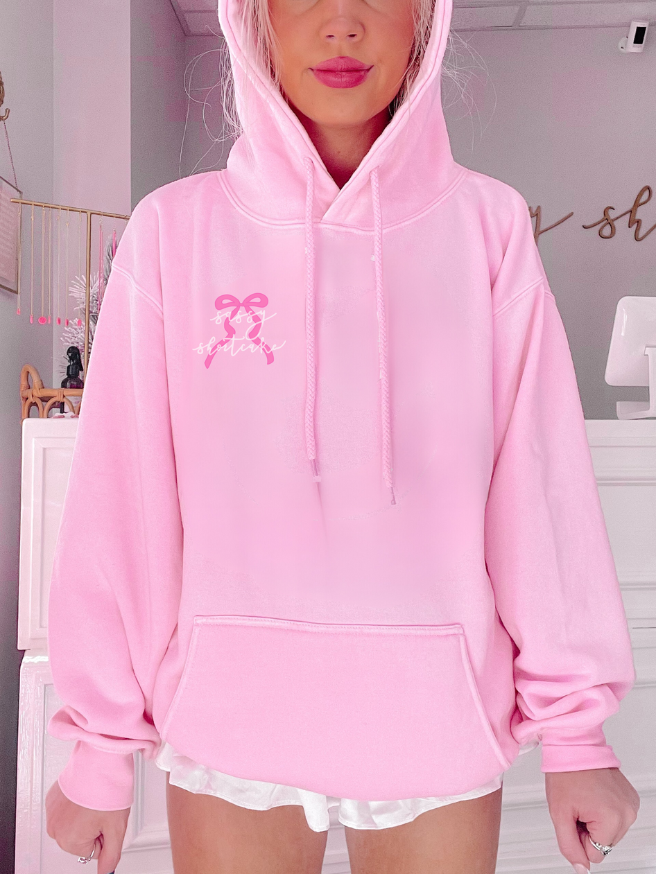 Pink hoodie featuring a cute bow and script design, shown on a model.
