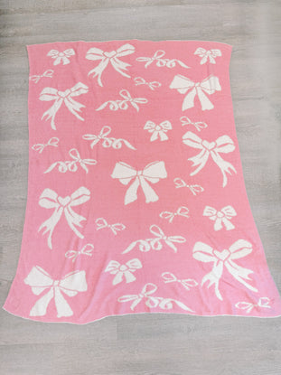 Pink knit throw blanket with a white bow pattern.
