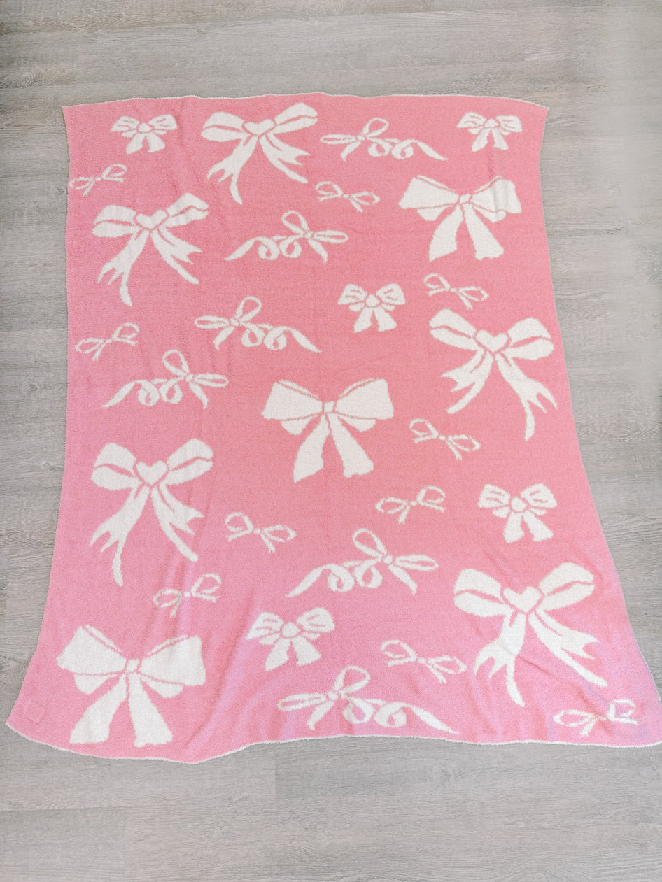 Pink knit throw blanket with a white bow pattern.
