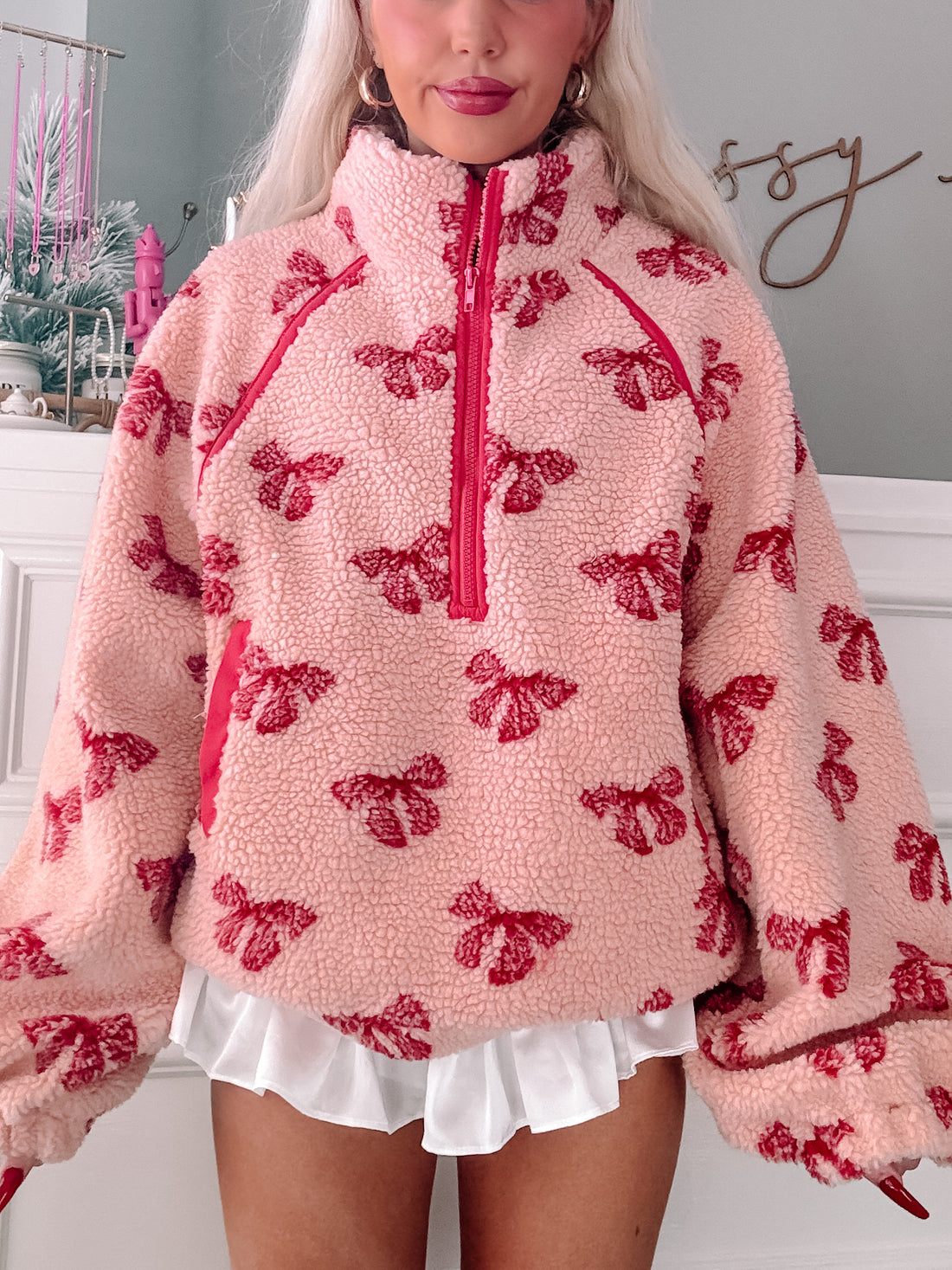 Pink sherpa pullover with red bow pattern, half-zip closure.
