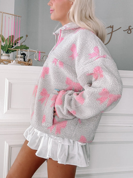 Grey and pink patterned sherpa pullover with a half-zip closure, shown paired with a white ruffled skirt.