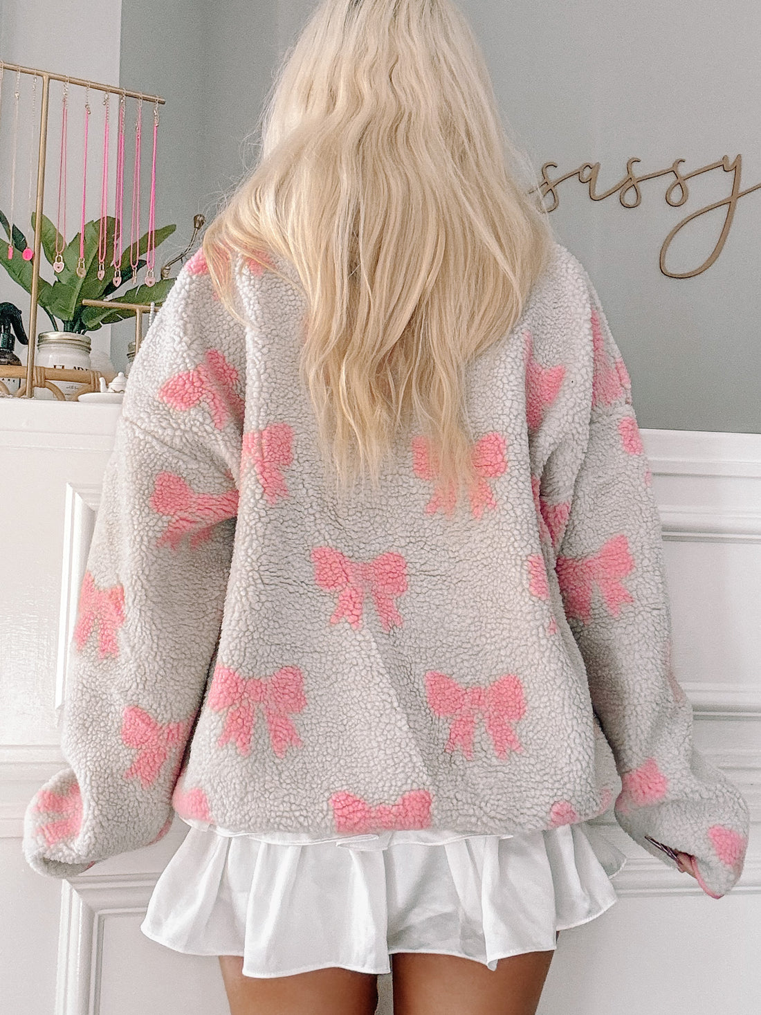 Light gray oversized sherpa pullover with pink bow print, modeled from the back.
