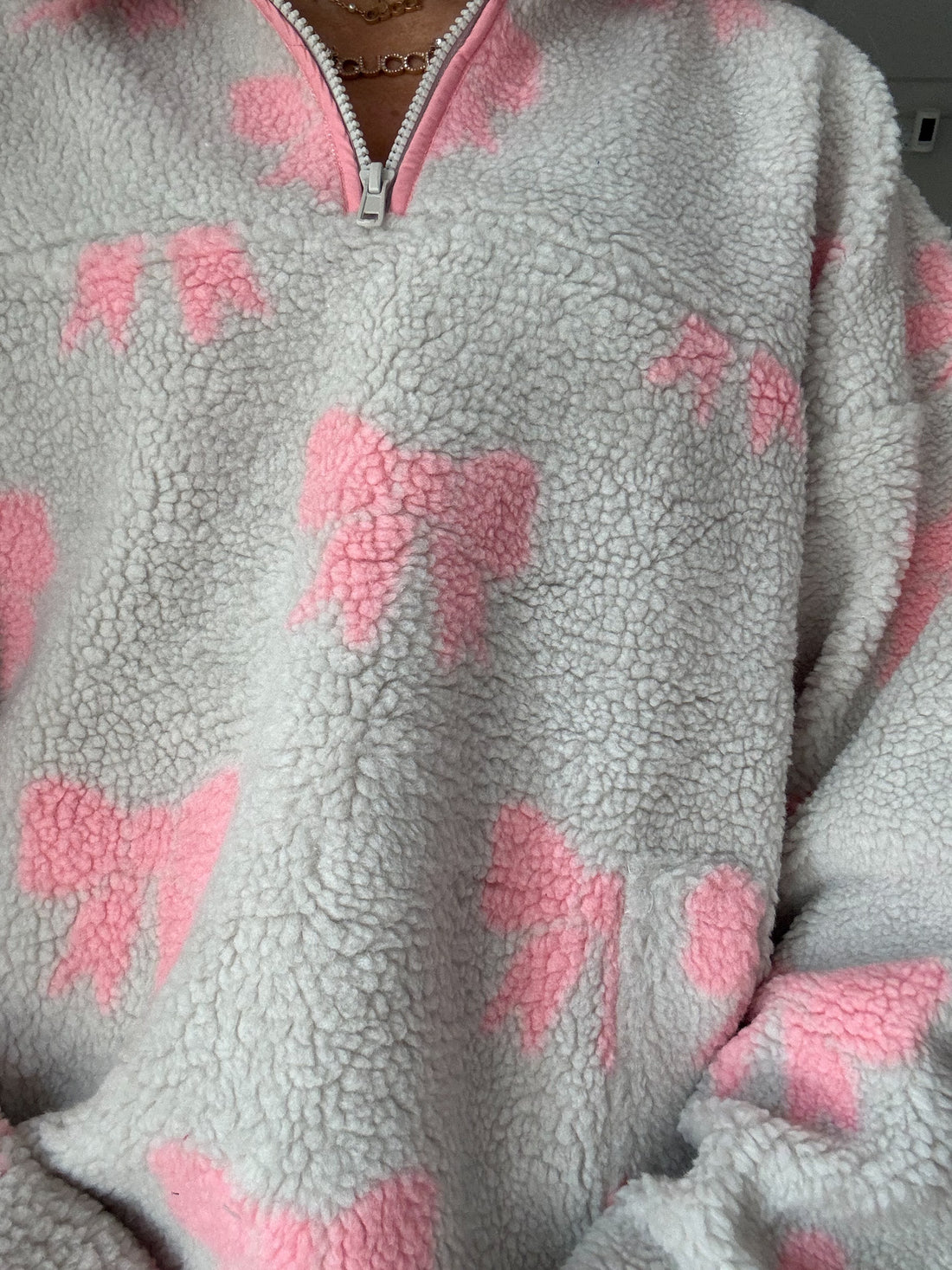 Grey sherpa pullover with pink bow pattern, half-zip closure.
