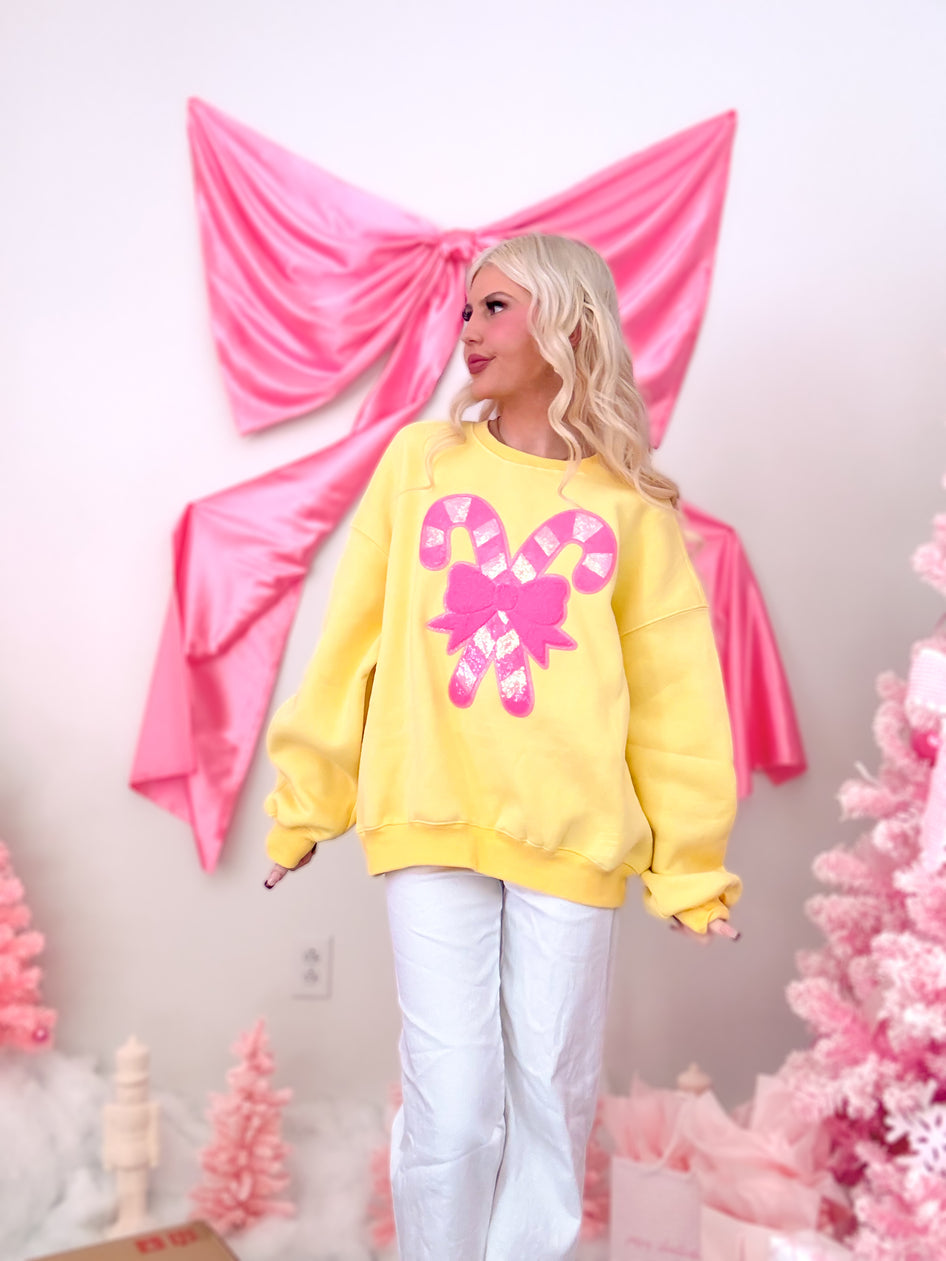 Sassy Shortcake Candy Cane Sequin Crewneck, a bright yellow sweatshirt featuring a sequin candy cane and neon pink bow design.