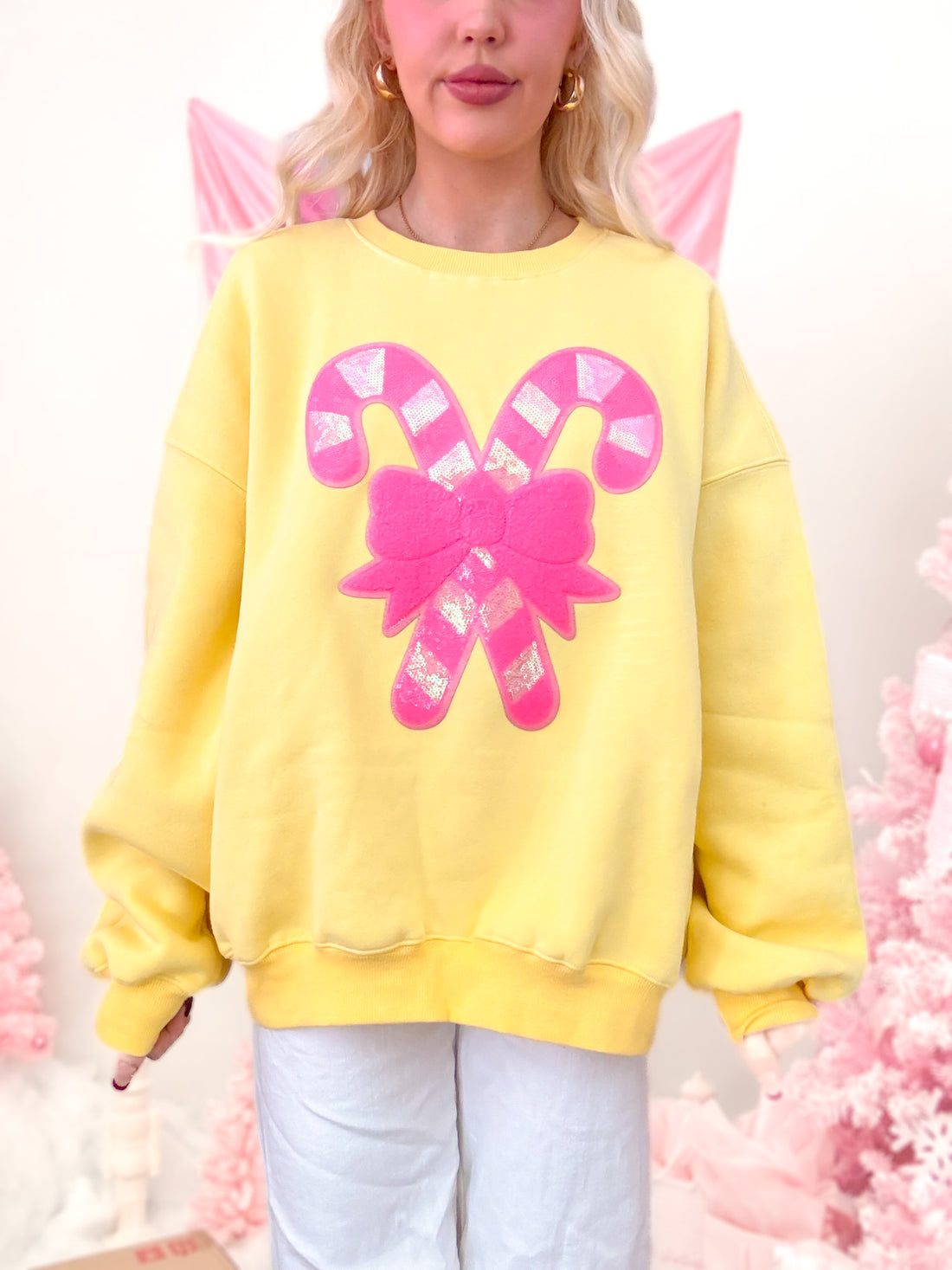 Close-up of the front of the yellow crewneck, highlighting the sparkly sequin candy cane and neon pink bow holiday design.