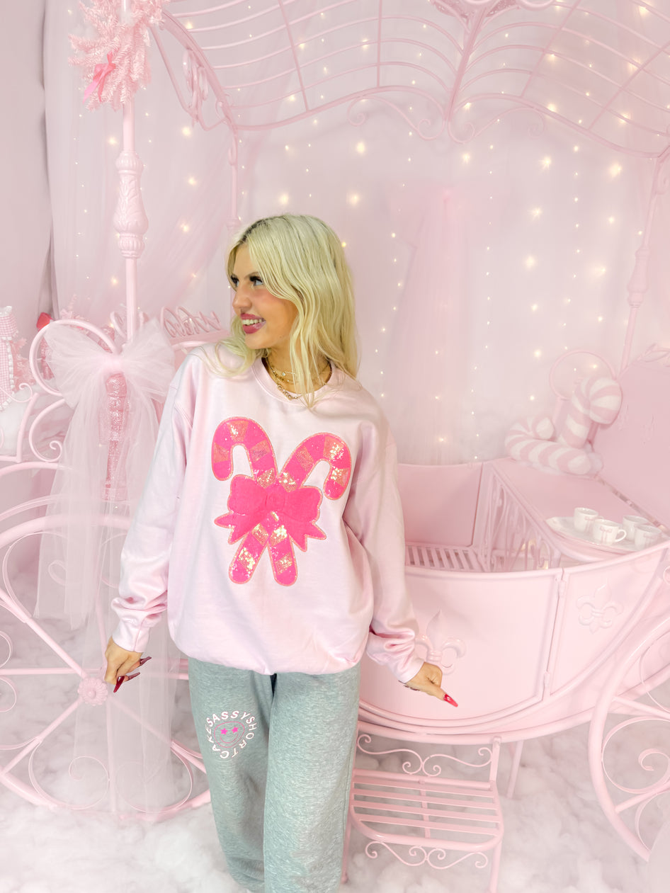 Pink candy cane sweatshirt with sequined detail, modeled in a whimsical pink setting.
