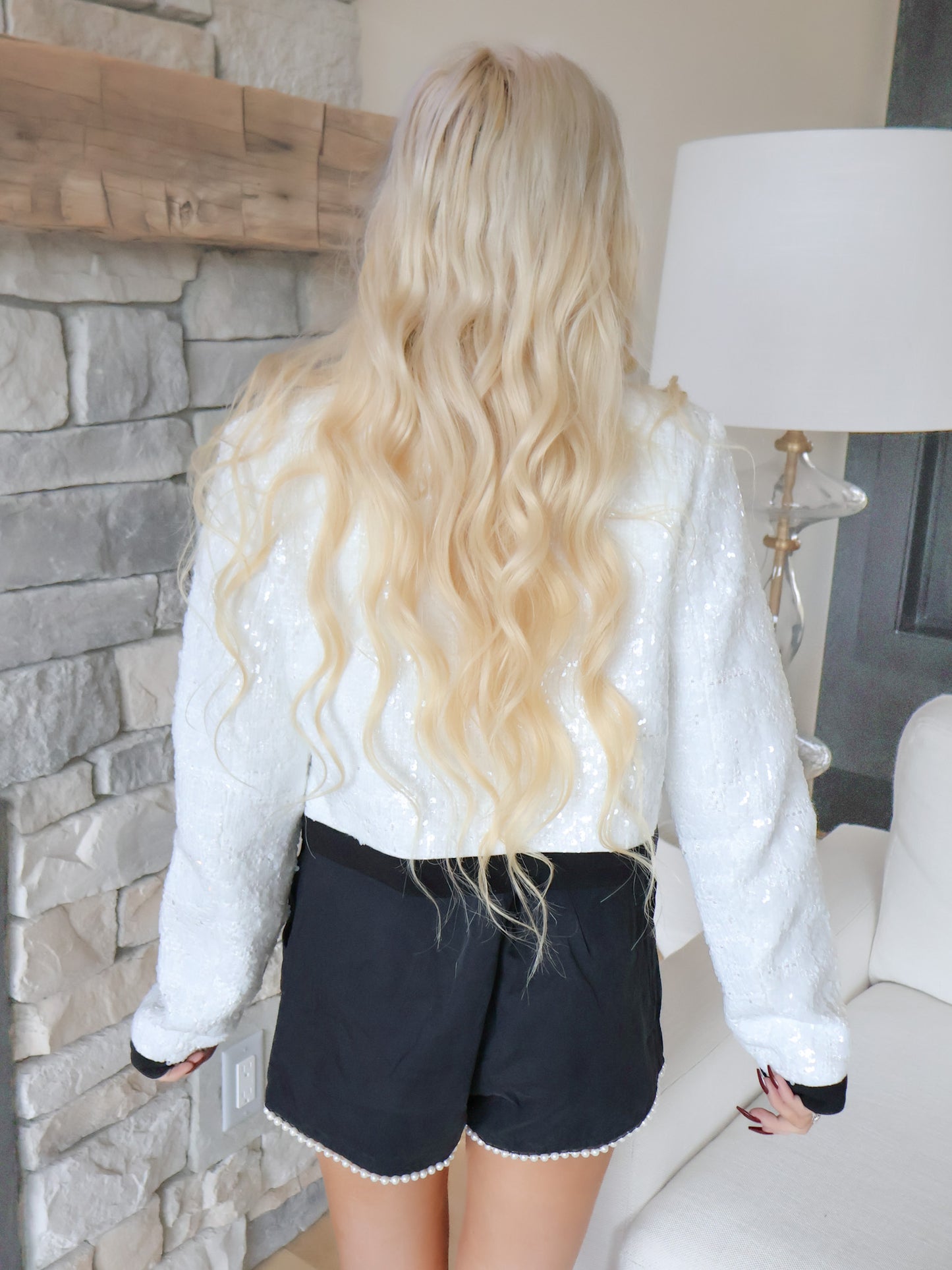 Person wearing a sassy shortcake white sweater and black shorts in a room with stone wall and lamp.