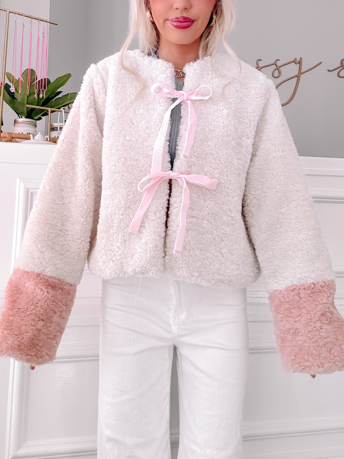 Cream sherpa jacket with blush pink cuffs, tied with a delicate pink ribbon.
