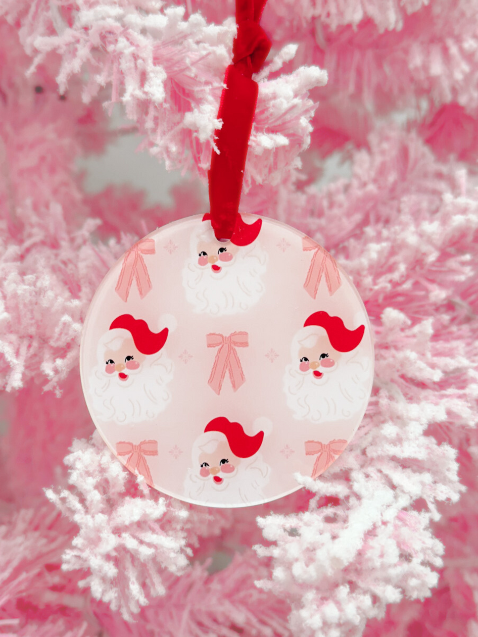 Pink round glass ornament featuring a repeating pattern of vintage Santa faces and pink bows, hanging on a pink tree.
