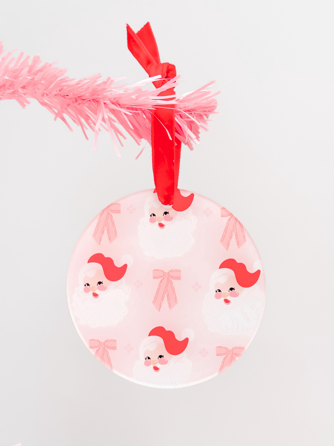 Pink Circle Santa Ornament with red ribbon, features repeating Santa pattern.
