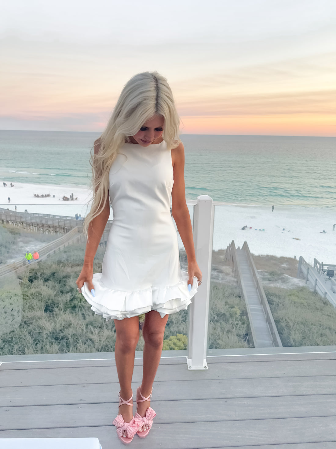 White mini dress with ruffled hem, worn on a beachside deck at sunset.
