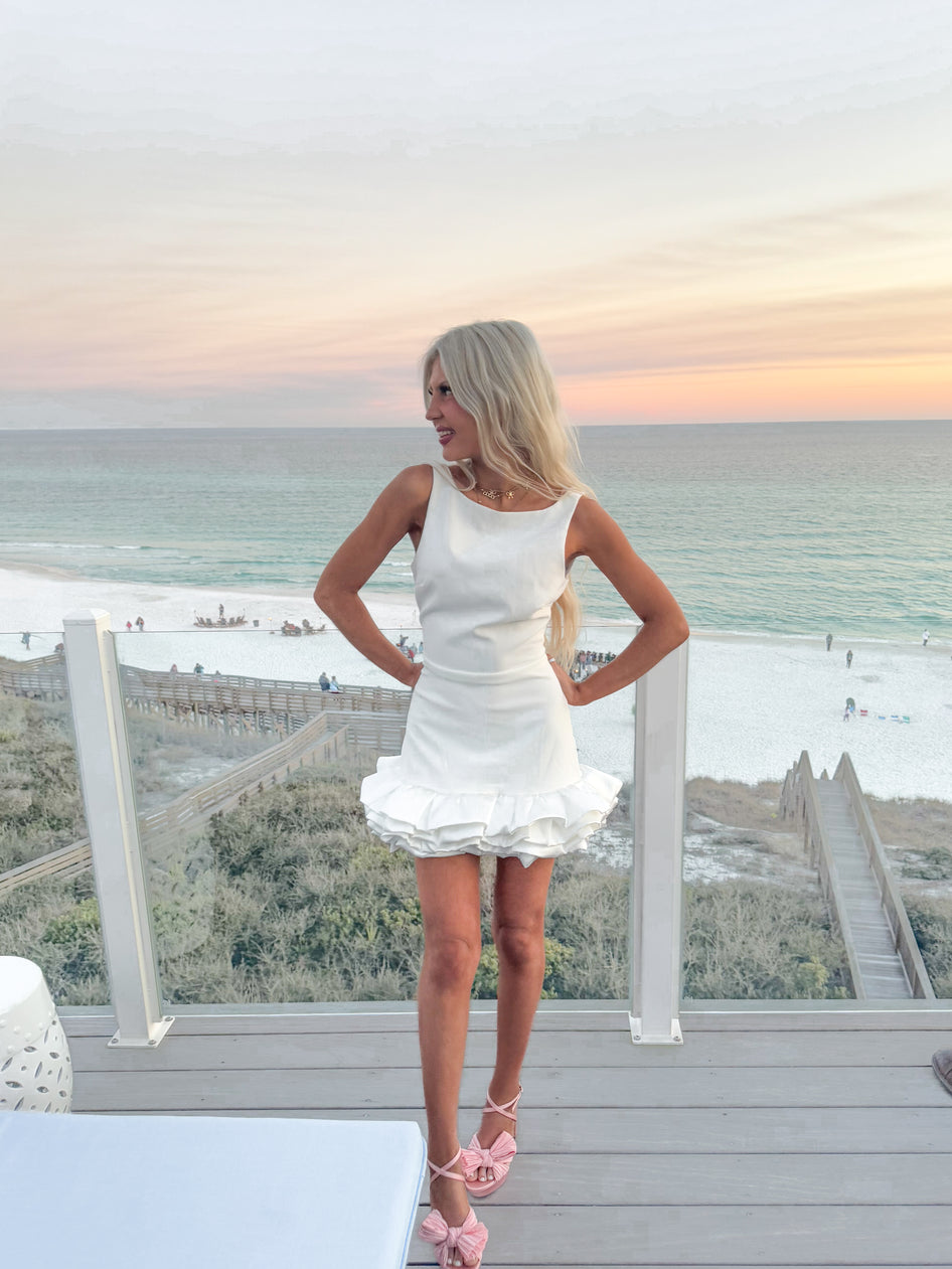 White ruffled mini dress overlooking ocean beach at sunset.
