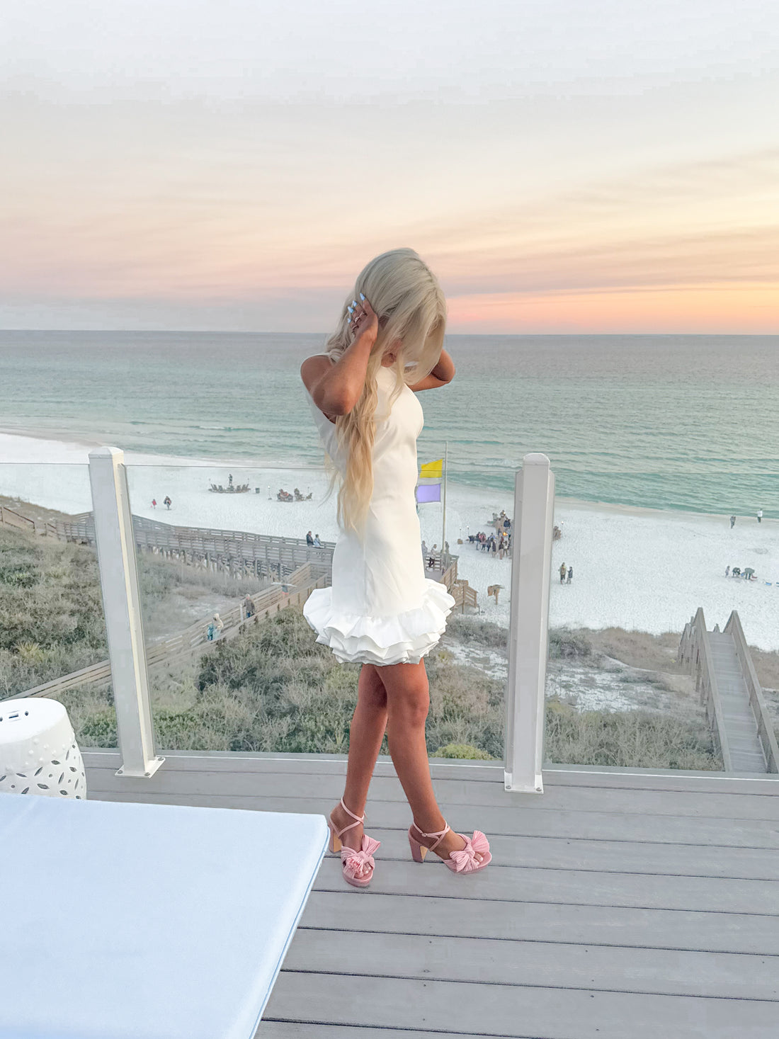 White ruffle-hem dress on a beachside deck at sunset.
