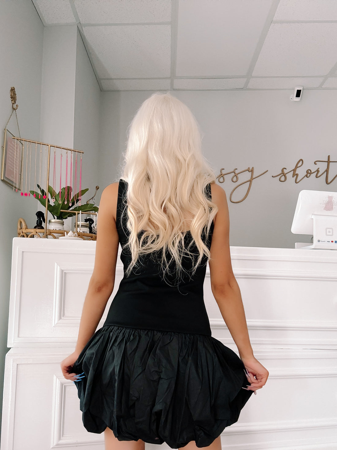 Black bubble hem mini dress, shown from the back in a boutique setting.
