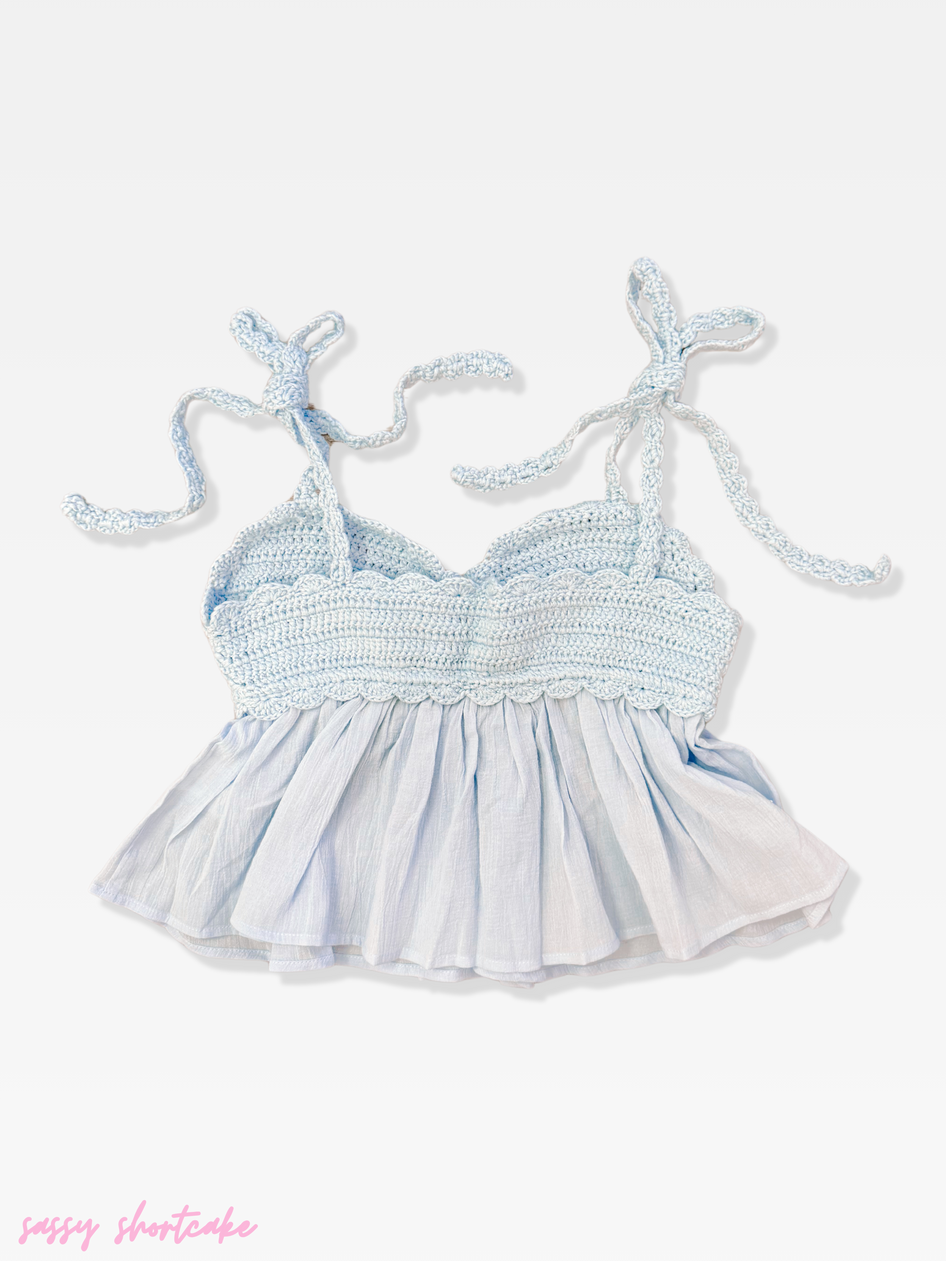 Light blue crocheted top with ruffled bottom and knotted straps, shown on white background.
