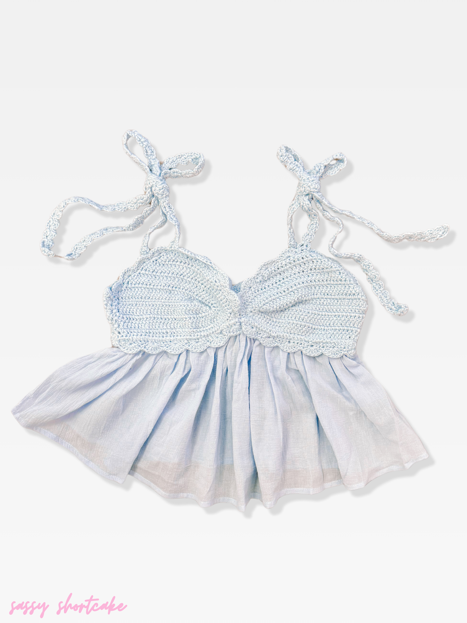 Light blue crochet top with fabric bottom and knotted straps, shown on white background.
