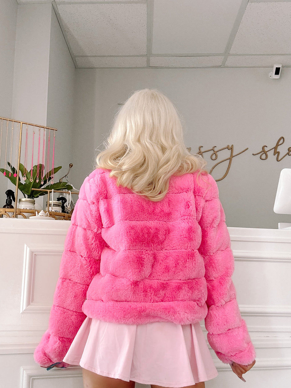 Hot pink fluffy faux fur coat, shown from the back in a bright interior setting.
