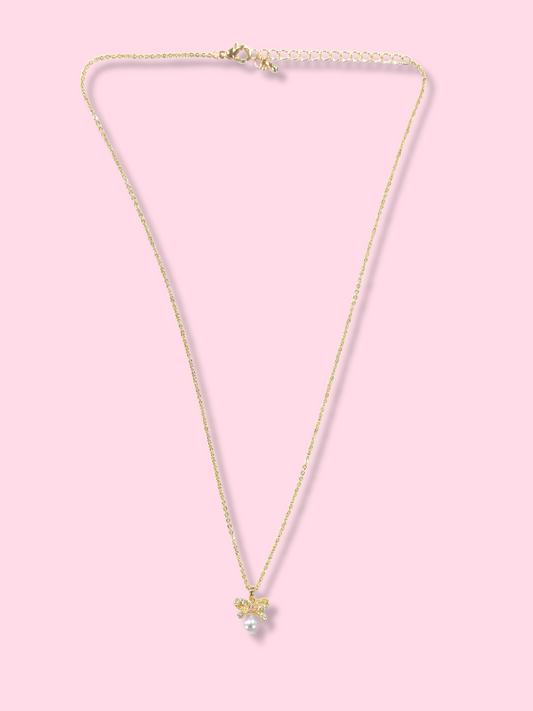Gold chain necklace with a dainty bow and pearl pendant, displayed against a pink background.