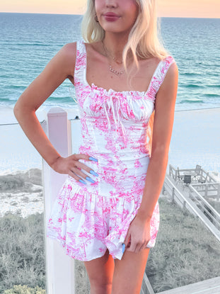Pink and white toile print mini dress, worn outdoors near the ocean.
