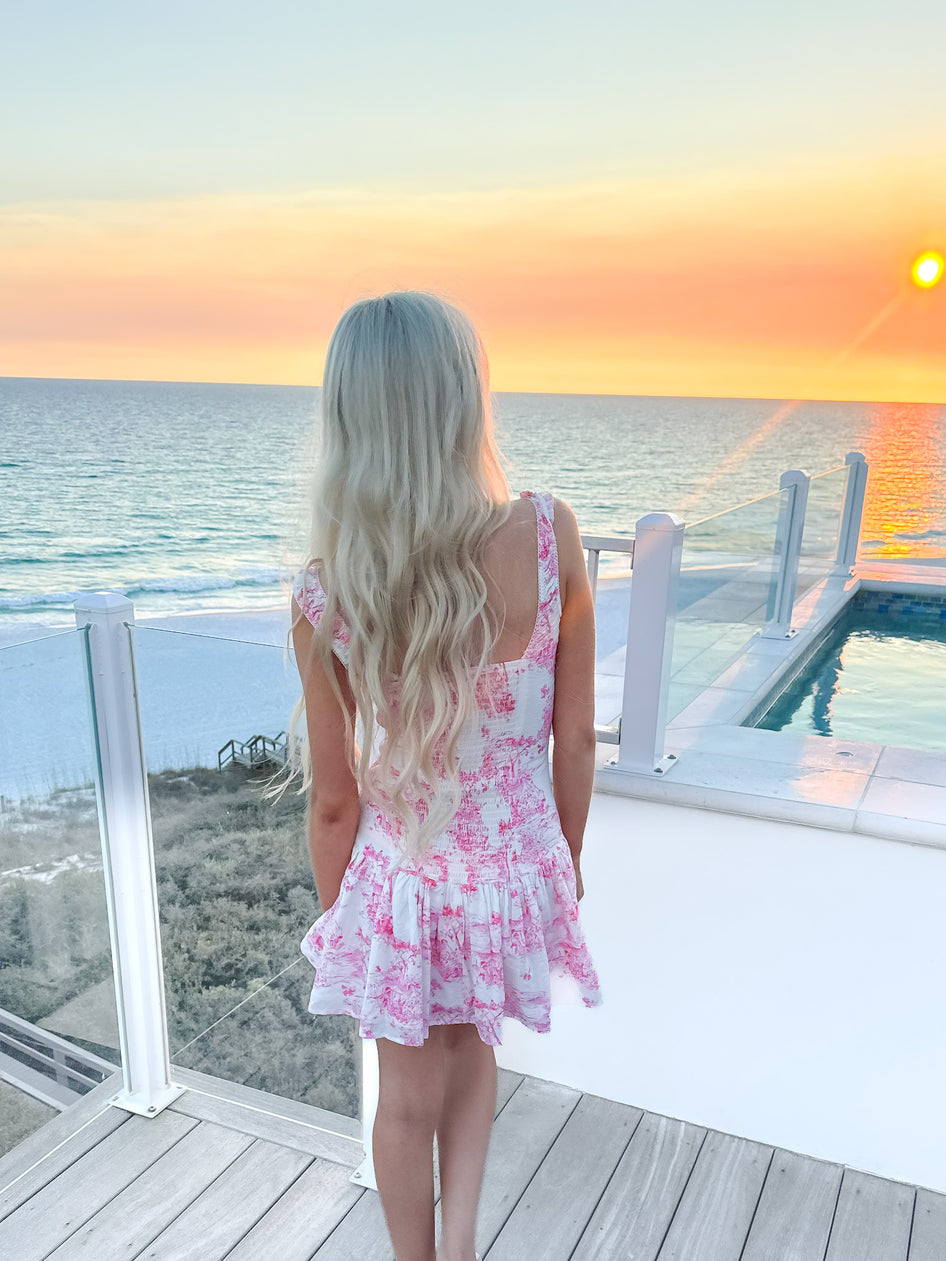 Pink floral dress viewed from behind, overlooking ocean sunset
