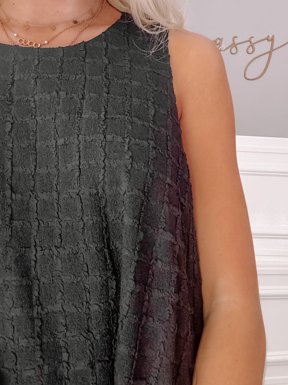 Close-up of dark gray textured sleeveless dress, showcasing fabric detail.
