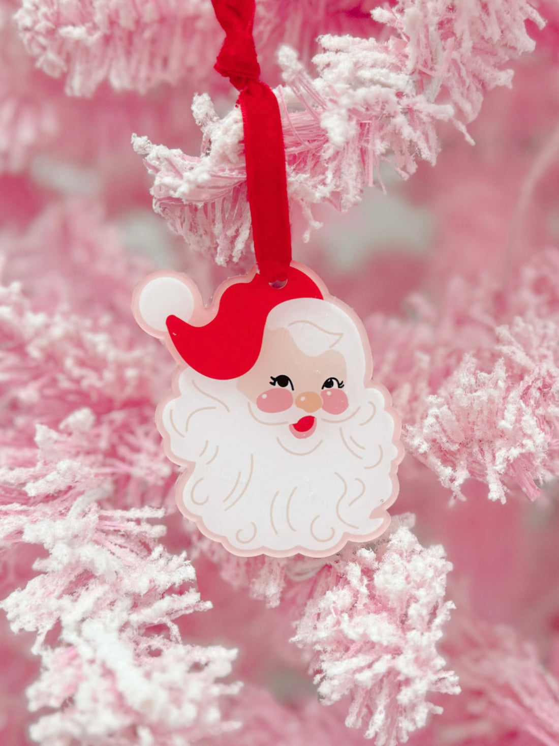 Pink acrylic Santa ornament hanging on a fluffy pink Christmas tree.
