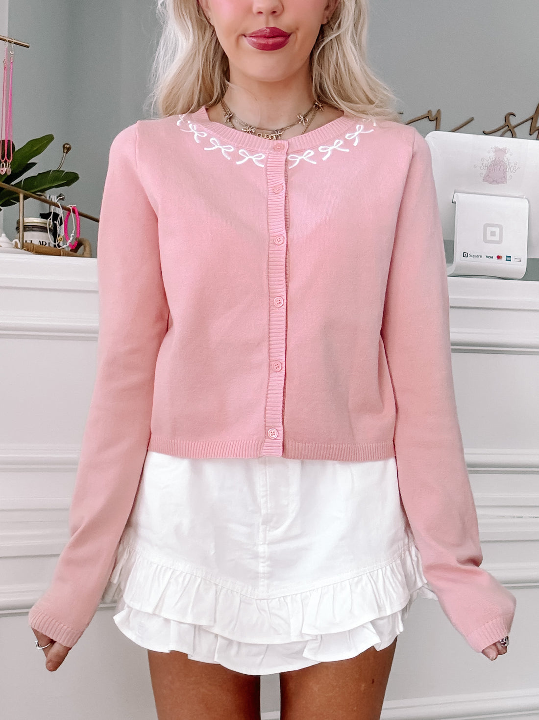 Pink button cardigan with delicate white embroidery, modeled with a white ruffle skirt.
